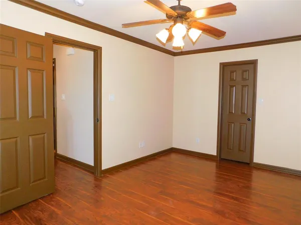 an empty room with a chandelier fan and wooden floor