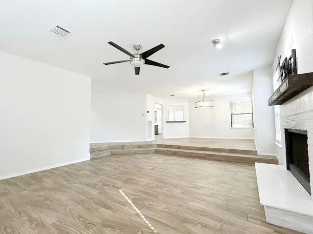a view of a livingroom with a fireplace a ceiling fan and wooden floor