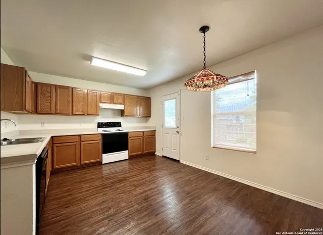 a kitchen with granite countertop a stove a sink dishwasher a refrigerator and wooden floor