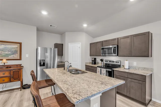 a kitchen with granite countertop stainless steel appliances a sink stove refrigerator and cabinets