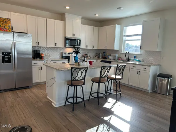 a kitchen with stainless steel appliances a dining table chairs refrigerator and sink