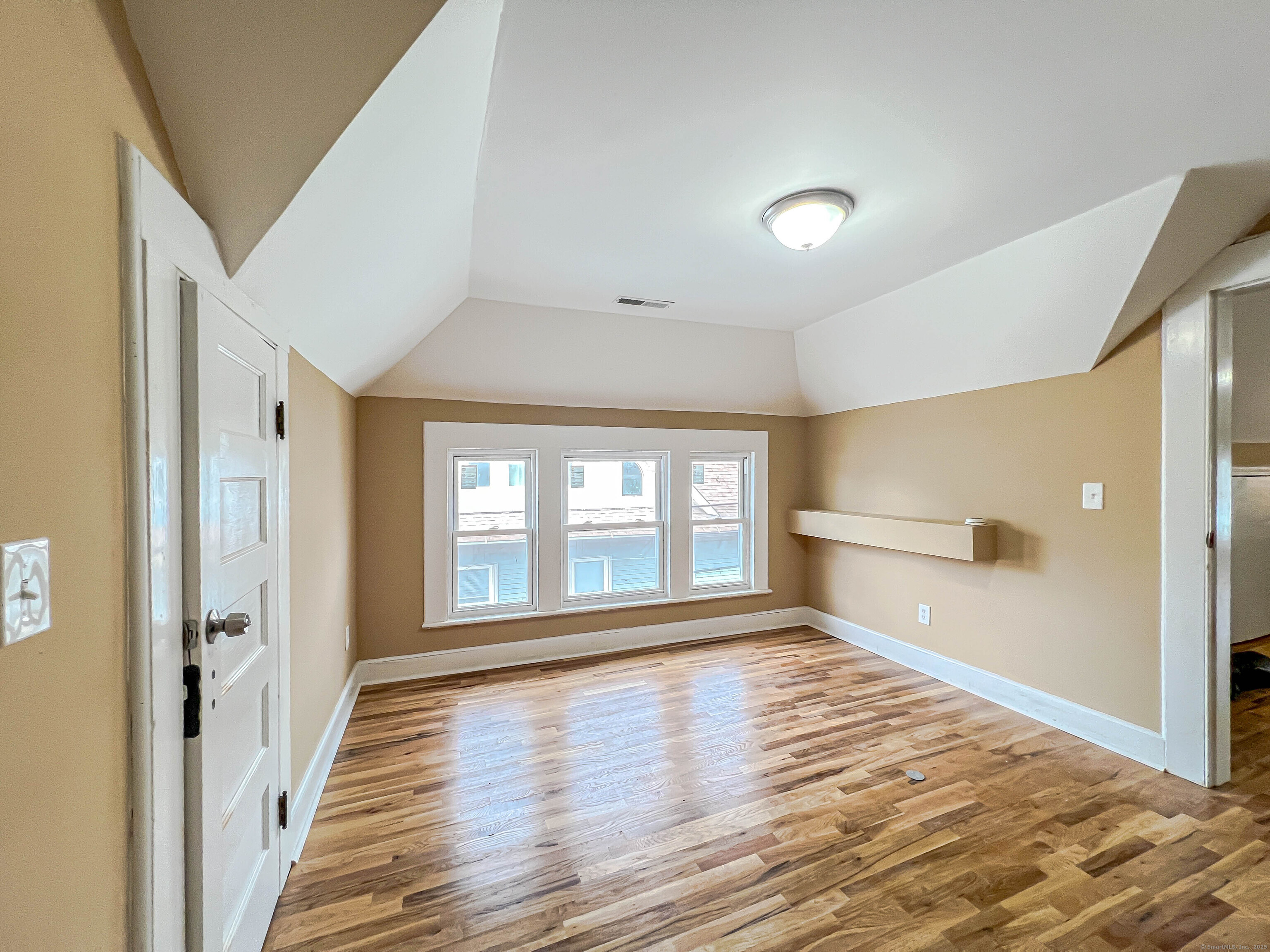 a view of an empty room with wooden floor and a window