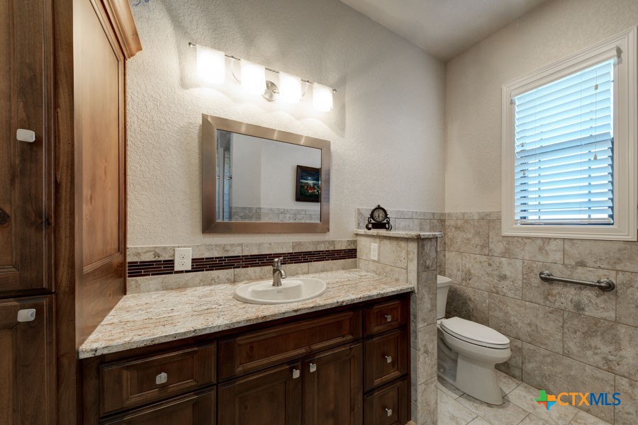 2420 Bolton Road Marion, TX 78124 - Photo 15 of 30 a bathroom with a granite countertop toilet a sink a mirror and a window