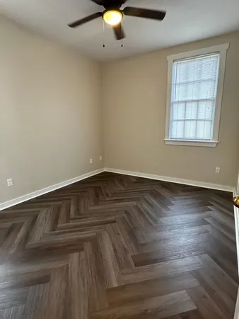 an empty room with wooden floor chandelier fan and windows