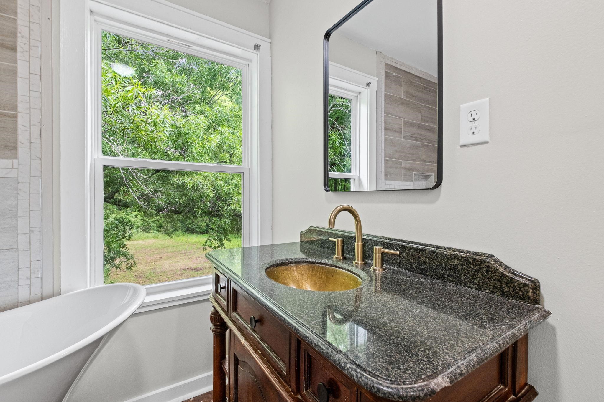 5843 Stewart Road Lakeland, TN 38002 - Photo 24 of 26 Freestanding soaking tub with a window, dark wood vanity with a speckled countertop, and a gold-finish vessel sink and faucet
