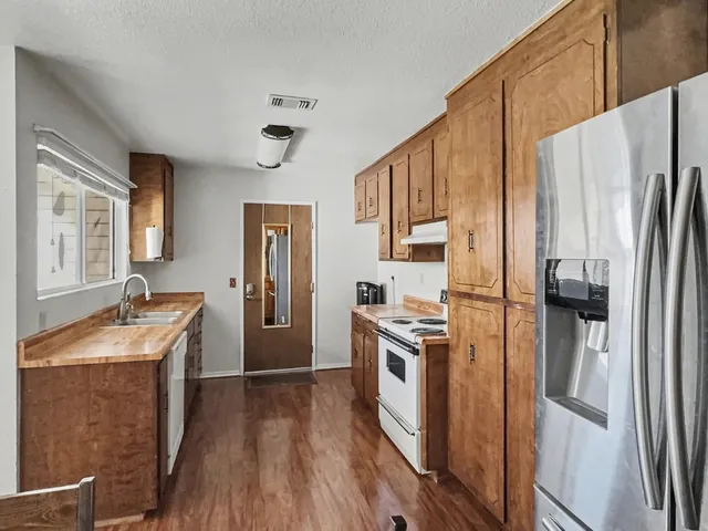 a kitchen with stainless steel appliances granite countertop a refrigerator a stove and a sink with wooden floors