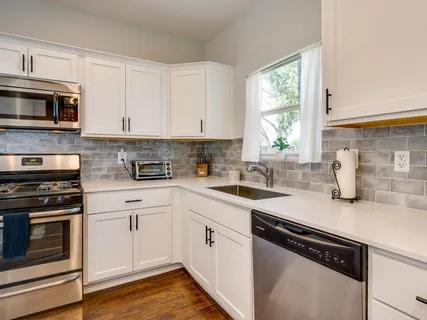 a kitchen with stainless steel appliances white cabinets a sink a stove a microwave and wooden floors