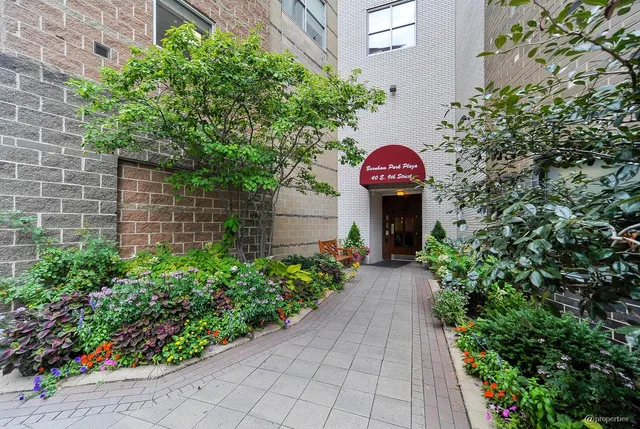a view of a pathway with flower plants and brick wall