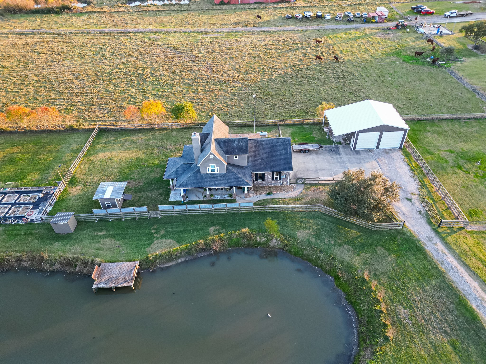 912 County Road 340 Angleton, TX 77515 - Photo 44 of 50 This aerial view showcases a charming country home with a spacious front porch, nestled by a small pond. The property features a large metal outbuilding, fenced areas, and expansive open land, offering a peaceful rural setting ideal for privacy and tranquility.