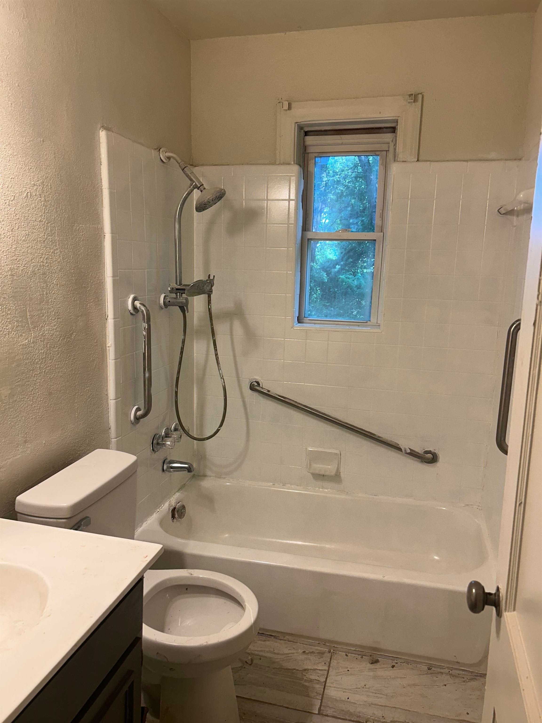 904 North Ball Road Memphis, TN 38106 - Photo 10 of 12 Bathroom featuring a white tiled shower surround, a white bathtub, and a window
