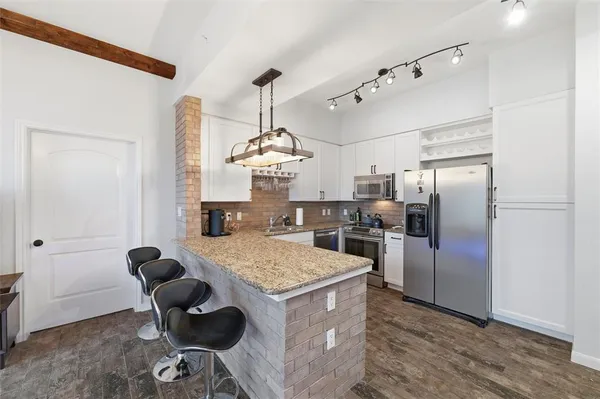 a kitchen with stainless steel appliances kitchen island granite countertop a refrigerator a stove a kitchen island a dining table and chairs with wooden floor