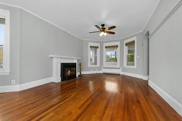 a view of an empty room with wooden floor fireplace and a window