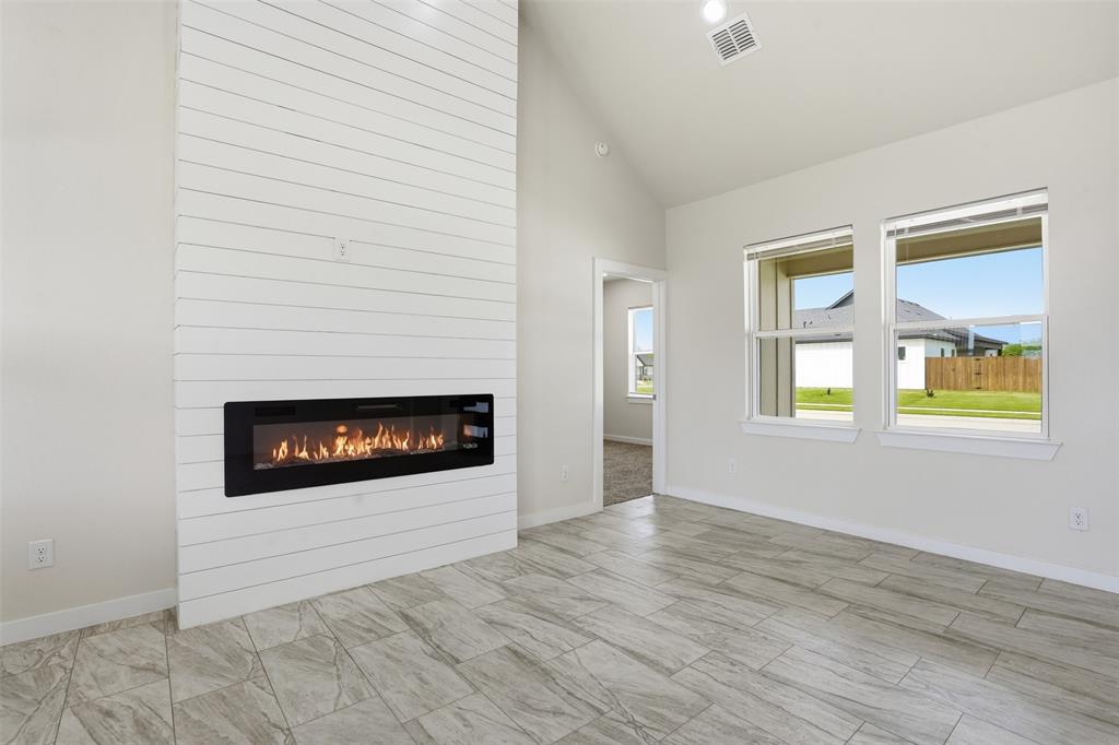 532 Highview Court Godley, TX 76044 - Photo 33 of 39 Living area featuring a floor-to-ceiling shiplap accent wall with a built-in linear electric fireplace, two large windows, wood-finish tile flooring, and vaulted ceiling