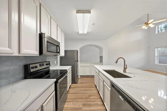 a kitchen with stainless steel appliances a sink dishwasher a stove top oven a refrigerator with white cabinets and wooden floor