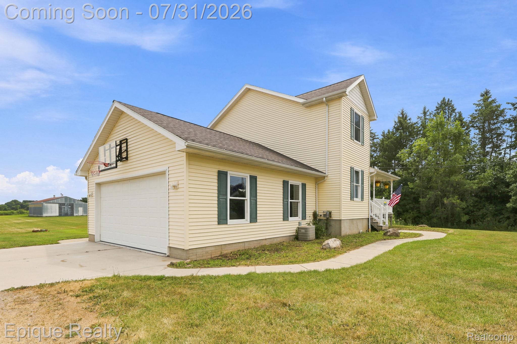 10179 Duffield Road Gaines, MI 48436 - Photo 2 of 30 Exterior featuring light yellow siding, dark green window shutters, a two-car garage with a white door, a paved driveway, and a concrete walkway