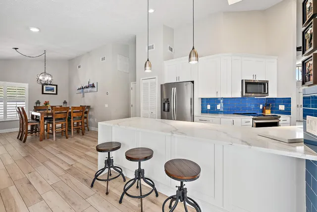 a kitchen with stainless steel appliances kitchen island granite countertop a dining table chairs and a refrigerator