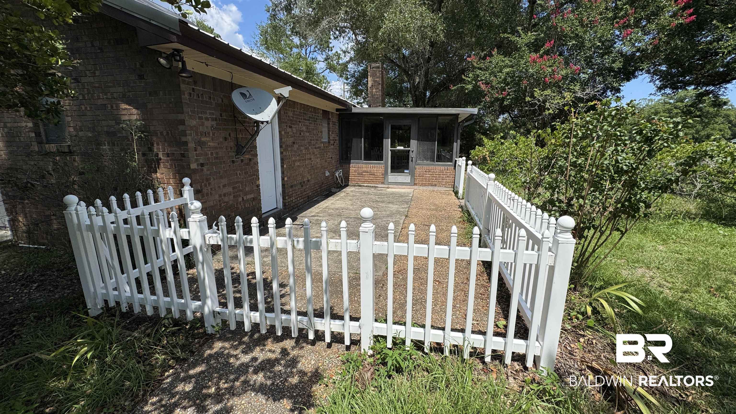 33370 Highway 98 Lillian, AL 36549 - Photo 9 of 58 Brick exterior with a covered patio area, featuring a white picket fence enclosure and a screened-in porch