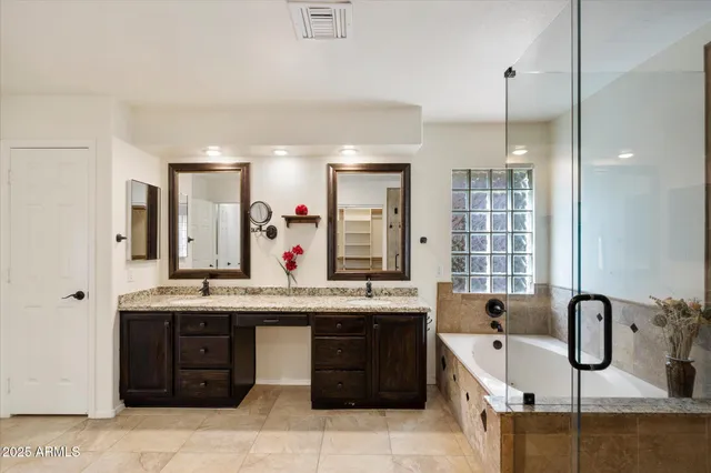 a bathroom with a granite countertop double vanity sink mirror bathtub and shower