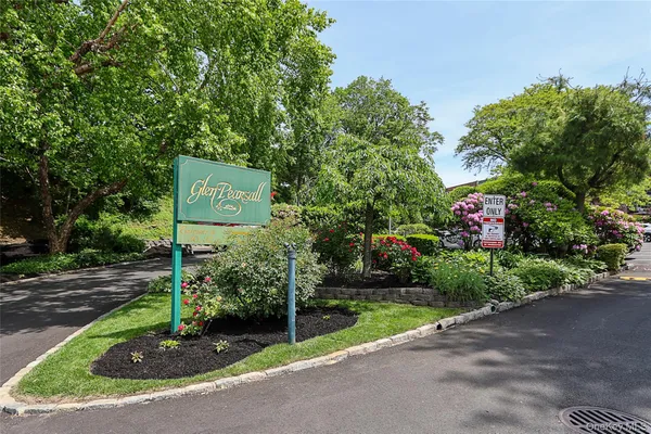 a sign board with flower plants and large trees