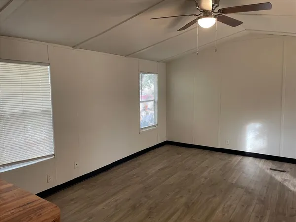 an empty room with wooden floor fan and windows