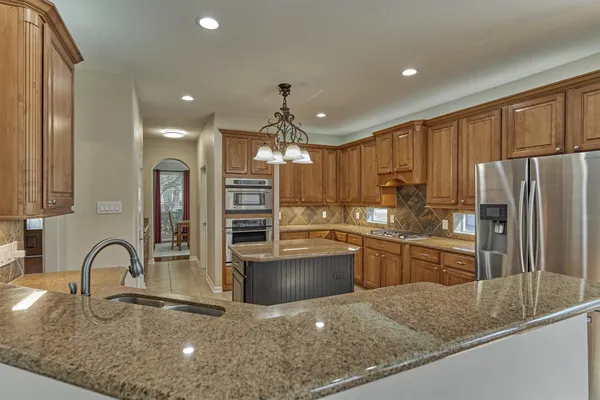 a kitchen with granite countertop a refrigerator a stove top oven and cabinets