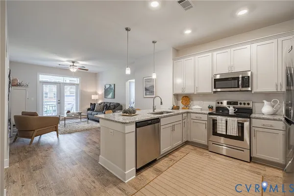 a kitchen with stainless steel appliances granite countertop a stove top oven a sink dishwasher a dining table and chairs with wooden floor