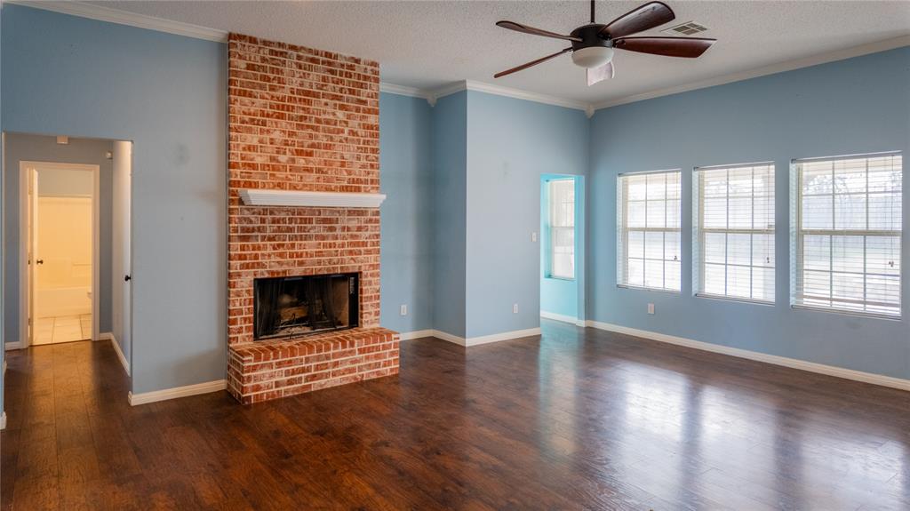 124 Topaz Circle Hewitt, TX 76643 - Photo 4 of 29 Unfurnished living room with crown molding, a brick fireplace, dark wood-style floors, a ceiling fan, and a textured ceiling