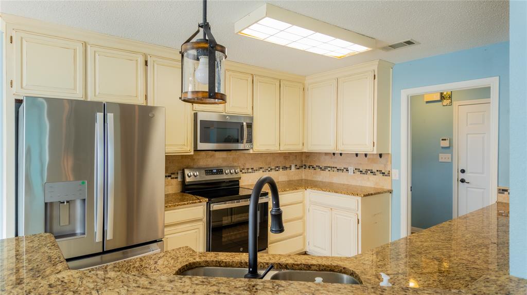 124 Topaz Circle Hewitt, TX 76643 - Photo 10 of 29 Kitchen featuring stainless steel appliances, a textured ceiling, cream cabinetry, light stone counters, and hanging light fixtures