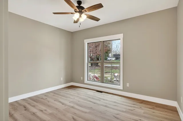 an empty room with wooden floor chandelier fan and windows
