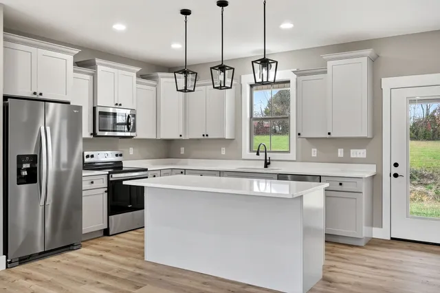 a kitchen with stainless steel appliances granite countertop a sink a stove a refrigerator and island with wooden floor