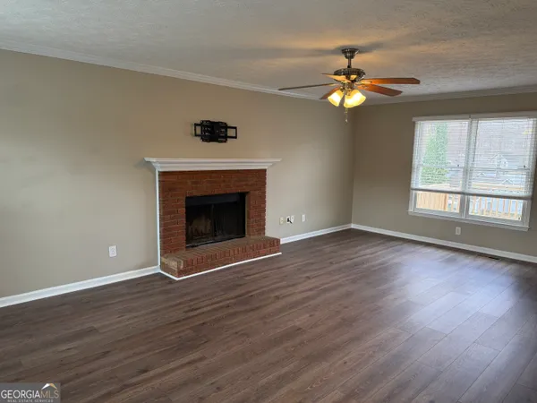 a view of an empty room with wooden floor fireplace and a window