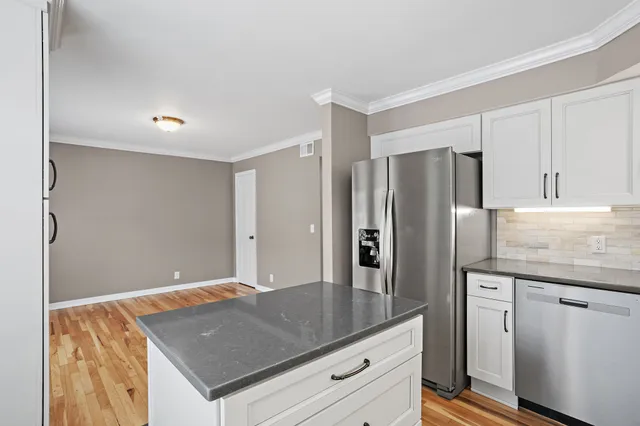 a kitchen with stainless steel appliances granite countertop a refrigerator a sink and white cabinets