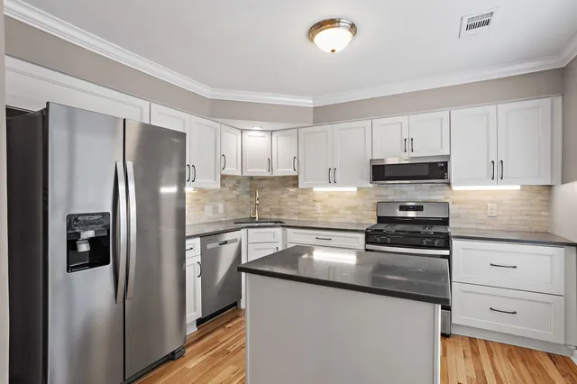 a kitchen with granite countertop a refrigerator stove and white cabinets