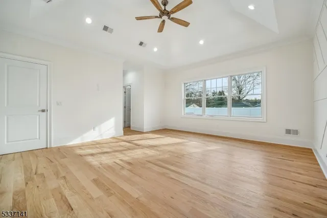 an empty room with wooden floor chandelier fan and windows