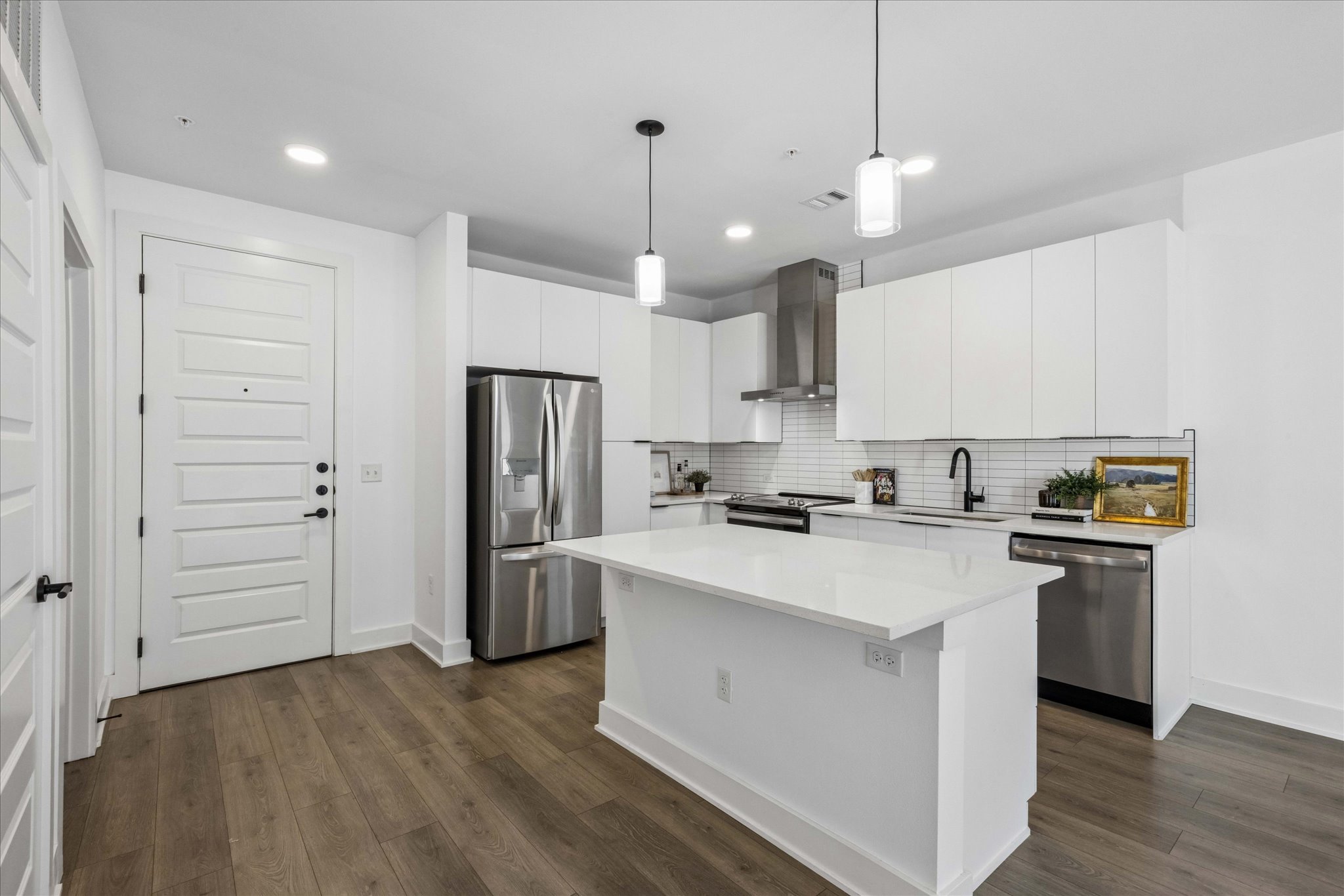 2220 Webberville Road, Unit 216 Austin, TX 78702 - Photo 3 of 26 Kitchen featuring a center island with a light-toned countertop, stainless steel appliances, a tile backsplash, white cabinetry, and wood-finish flooring