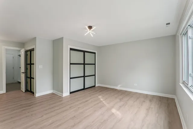 an empty room with wooden floor closet and windows
