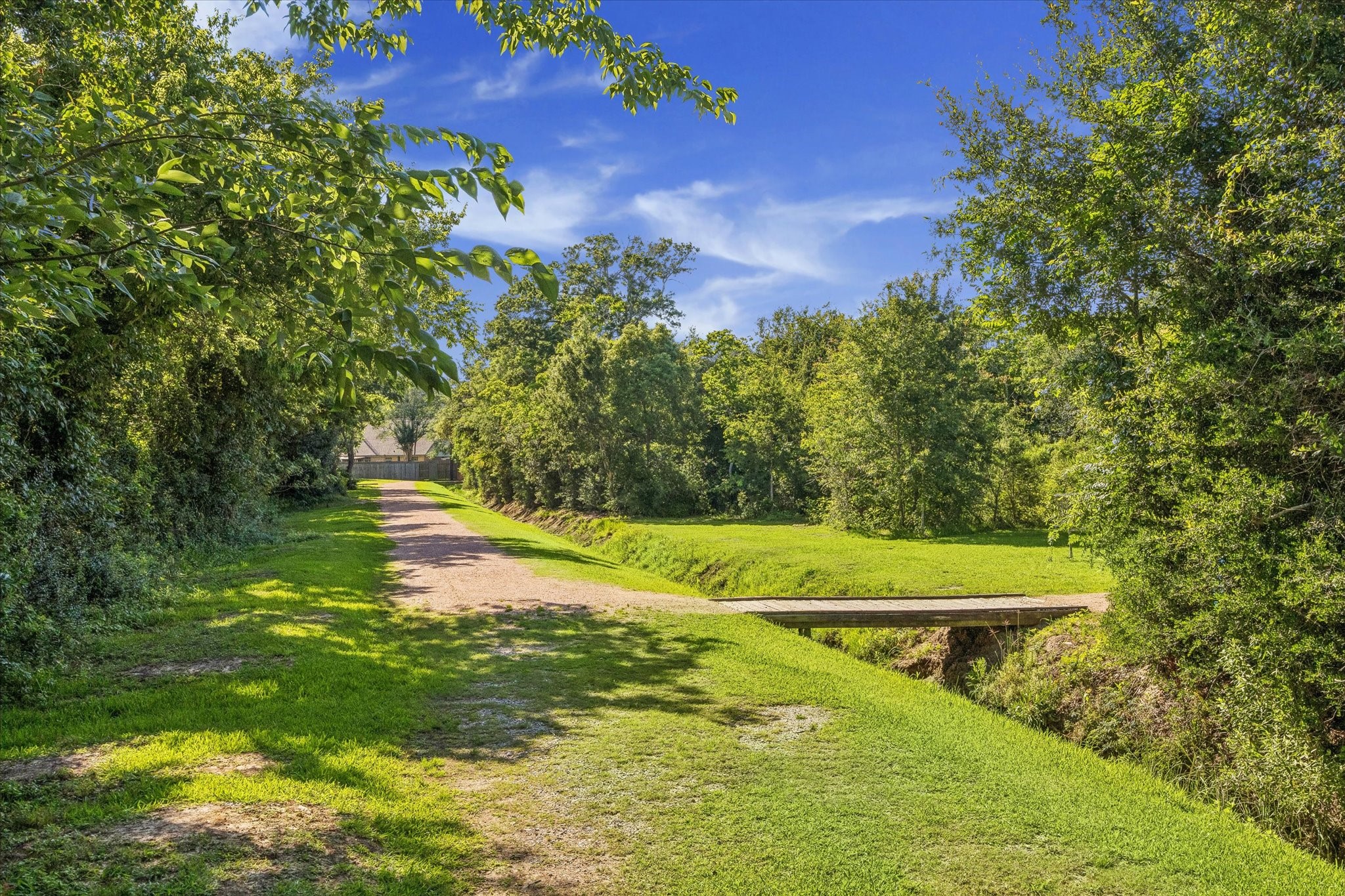 0 Hester Street Seabrook, TX 77586 - Photo 8 of 16 A picturesque rural pathway lined with lush greenery and trees, leading to a small wooden bridge under a clear blue sky. Perfect for nature lovers seeking tranquility.