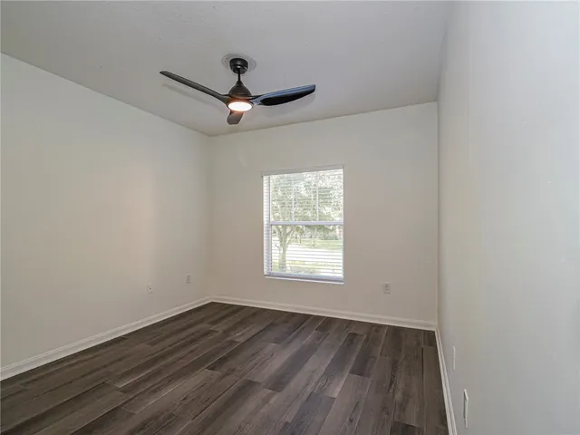 an empty room with wooden floor a ceiling fan and windows