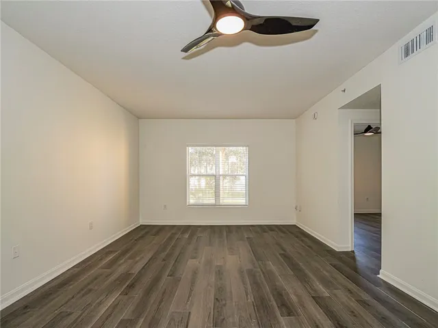 an empty room with wooden floor fan and windows