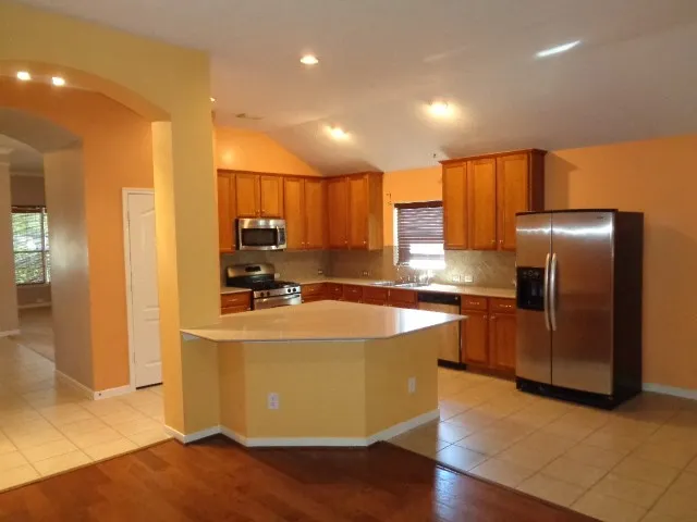 a large kitchen with stainless steel appliances wooden floor and a refrigerator