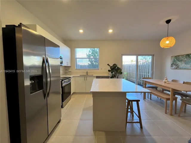 a kitchen with stainless steel appliances kitchen island granite countertop a refrigerator a stove a sink a dining table and chairs