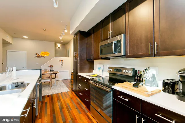 a kitchen with stainless steel appliances granite countertop a sink a stove top oven a chimney cabinets and a dining table