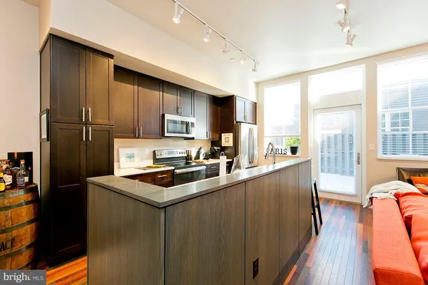 a kitchen with stainless steel appliances granite countertop a refrigerator a sink dishwasher a stove and white countertops with wooden floor