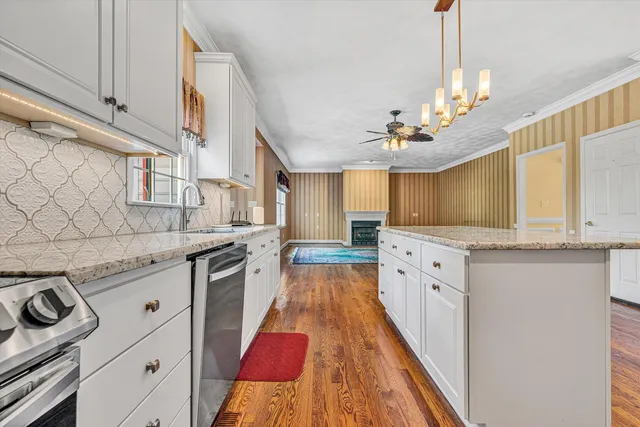 a kitchen with stainless steel appliances granite countertop a refrigerator a sink dishwasher a stove and white countertops with wooden floor