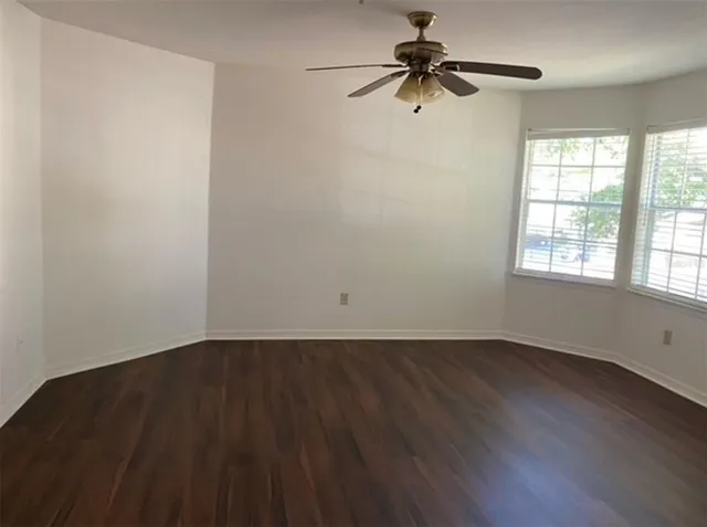 an empty room with wooden floor fan and windows