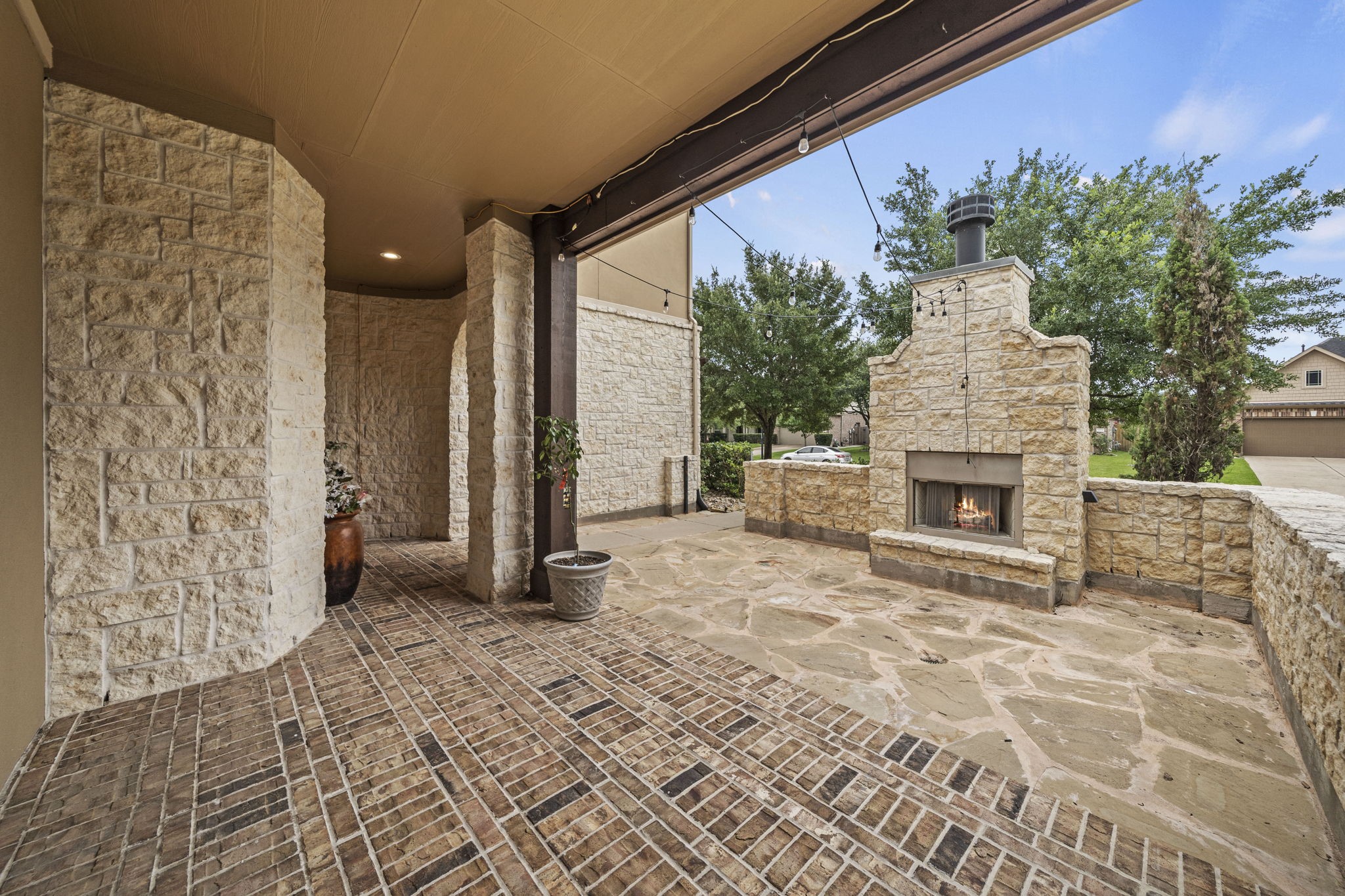 14215 Spindle Arbor Road Cypress, TX 77429 - Photo 2 of 47 This photo showcases an inviting outdoor space featuring a stone patio with a cozy built-in fireplace. The area is accented with brick flooring and lush greenery, creating an ideal setting for relaxation and entertaining.
