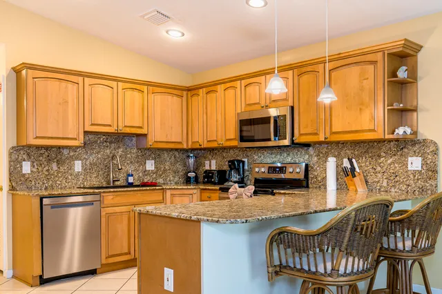 a kitchen with stainless steel appliances kitchen island granite countertop a stove a sink a refrigerator and chairs