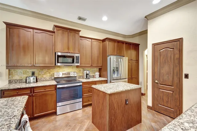 a kitchen with stainless steel appliances granite countertop a refrigerator a sink dishwasher and wooden cabinets with wooden floor