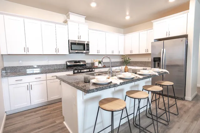 a kitchen with stainless steel appliances granite countertop a sink a stove a refrigerator cabinets and dining table