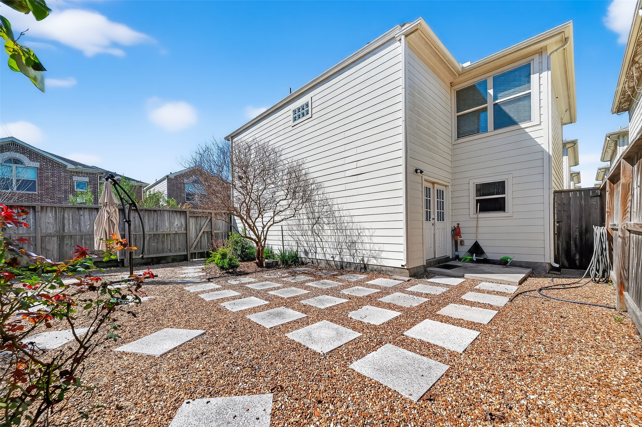 5951 S Loop East, Unit 47 Houston, TX 77033 - Photo 33 of 37 This photo showcases a private backyard with a modern, low-maintenance design, featuring a gravel area with stepping stones, a wooden fence, and minimal landscaping. The exterior of the house is light-colored, with large windows offering ample natural light. Ideal for outdoor relaxation.